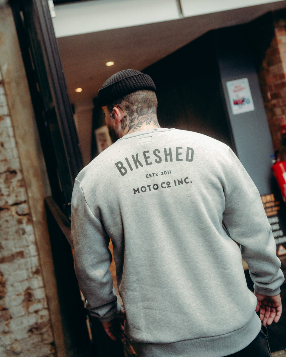 Model wearing Grey Bike Shed Moto Co ESTD Logo Sweatshirt on brick driveway