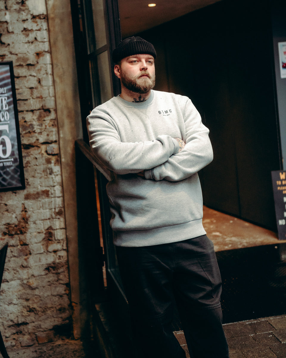 Model wearing Grey Bike Shed Moto Co ESTD Logo Sweatshirt on brick driveway