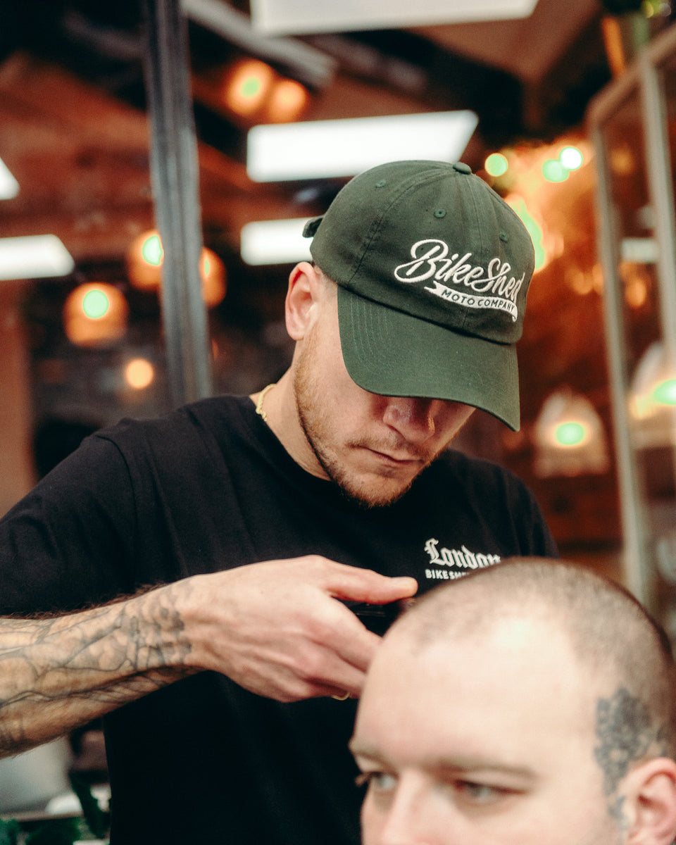 Model wearing Bike Shed Moto Script cap in green while cutting hair