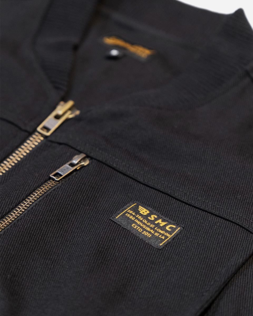 Black motorcycle vest with gold zipper and visible Bike Shed Moto Co brand logo on a white background