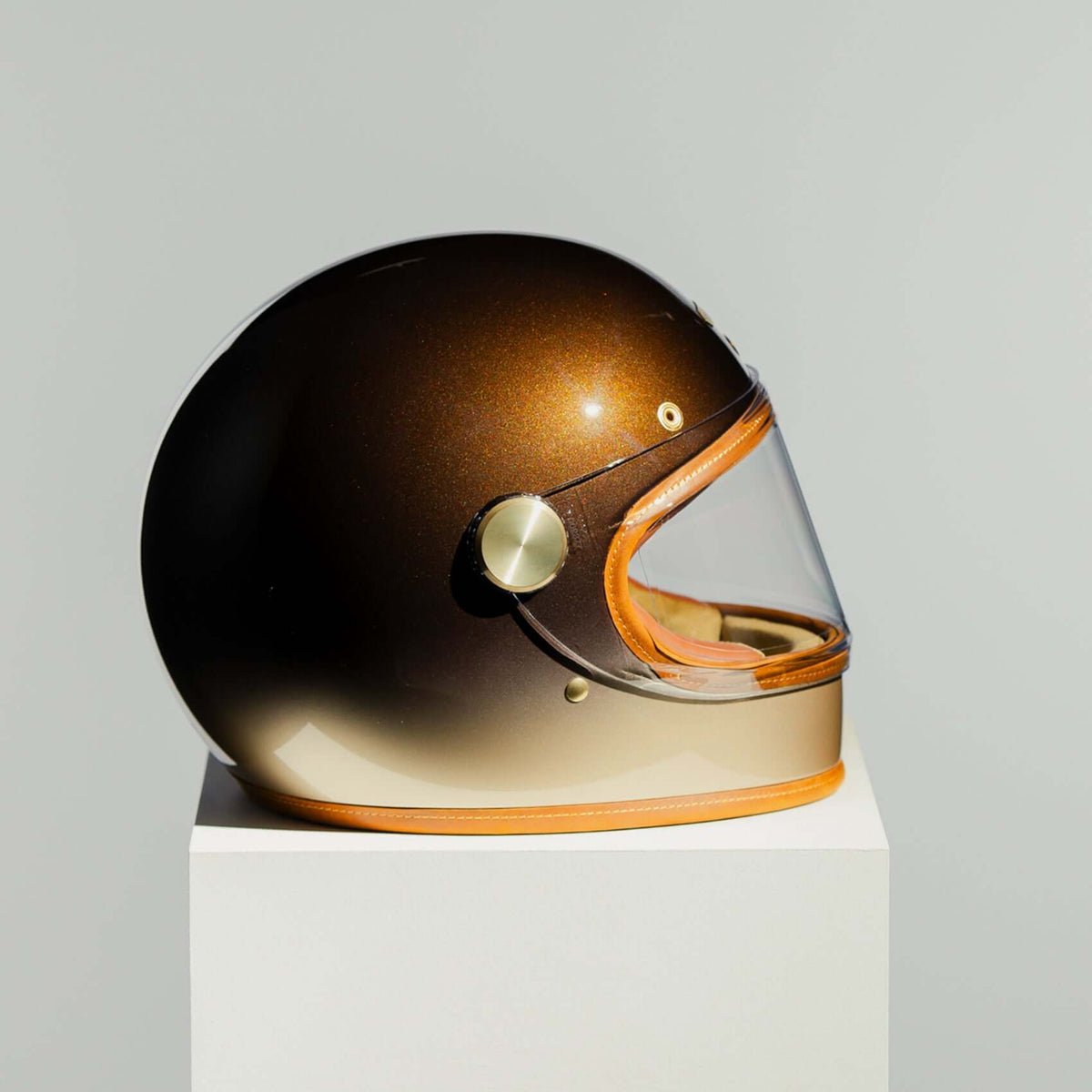 Gold and black helmet on a white pedestal with a gray background