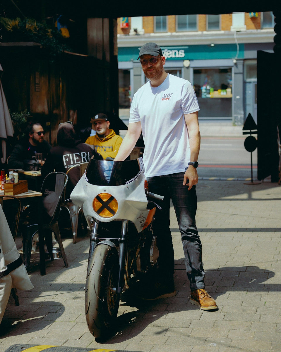 Model wearing Bike Shed Motorcycle Race T-Shirt White next to a custom motorcycle.