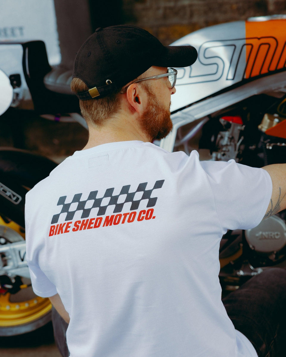 Model wearing Bike Shed Motorcycle Race T-Shirt White next to a custom motorcycle.